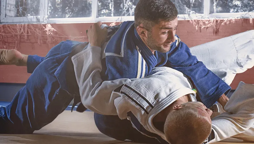 Judocy w białym i granatowym kimonie podczas walki w parterze na macie